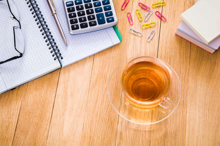 Cup of tea, notebook with pen, calculator and glasses on the desktop. Business concept