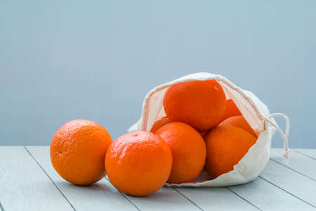 Fresh tangerines in a linen eco-bag on a light wooden tableの写真素材