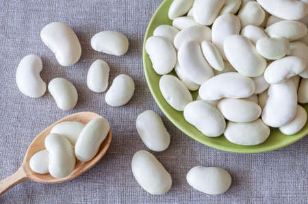 Large white beans on a plate and scattered on a linen cloth
