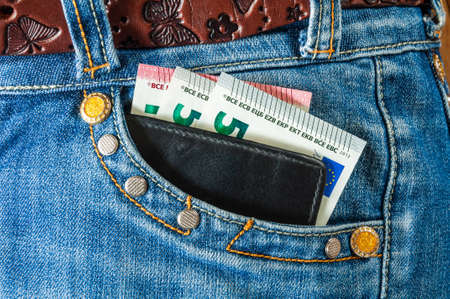 Black leather wallet with euro banknotes looks out of the pocket of jeansの写真素材