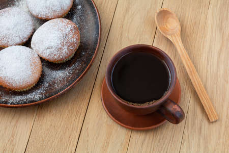 Fresh baked cupcakes sprinkled with powdered sugar and a cup of coffee on a wooden tableの写真素材