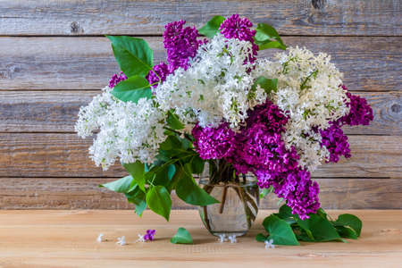 Bouquet of colorful lilac flowers in a glass vase on a wooden backgroundの写真素材