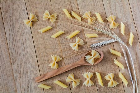 Raw farfalle and penne pasta on a wooden background. Top view ingredient of Italian cuisineの写真素材