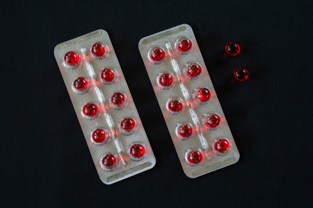Round red translucent pills in blister packs on a black background