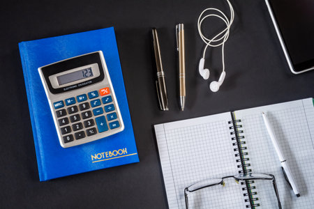 Notebook with pen, calculator and smartphone with headphones on black desktop. Accounting conceptの写真素材