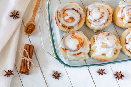 Delicious cinnamon buns covered with cream in a transparent baking tray on the tableの写真素材