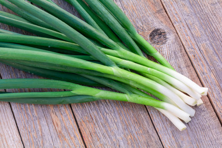 Bunch of fresh green onions on a feather on an old wooden tableの写真素材