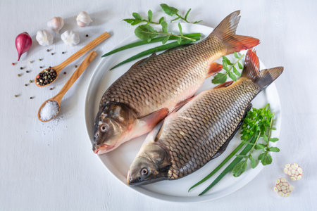 Fresh carp fish with herbs and spices on a plate on a white tableの写真素材