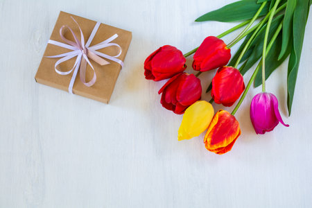 Beautiful bouquet of bright tulip flowers and gift box on white wooden background. copy spaceの写真素材