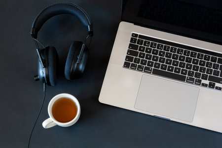 Workplace with a laptop with headphones and a cup of tea on a black desktopの写真素材