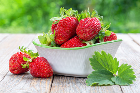Fresh ripe organic strawberries in a ceramic bowl on a wooden table outdoorsの写真素材
