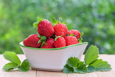 Fresh ripe delicious strawberries in a bowl on a wooden table outdoorsの写真素材
