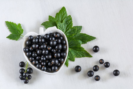 Currant berries in a white berry-shaped plate on a white wooden backgroundの写真素材