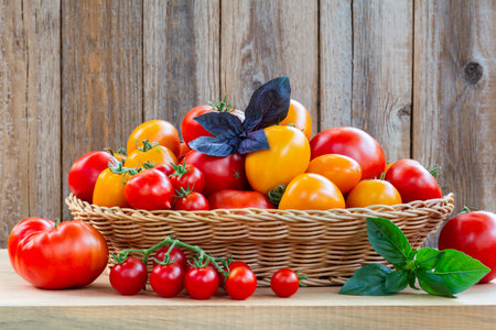 Fresh ripe tomatoes in a wicker basket on a wooden tableの写真素材