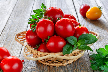 Fresh ripe tomatoes in a wicker plate on a wooden tableの写真素材
