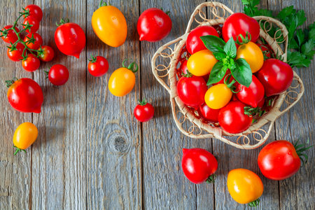 Fresh ripe red and yellow tomatoes in a wicker plate on a wooden tableの写真素材