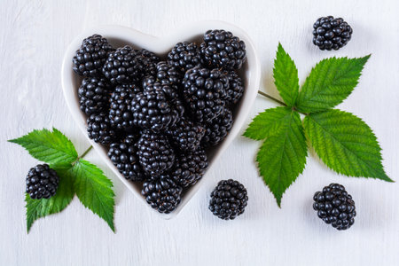 Blackberry berries in a white heart-shaped plate on a white wooden surfaceの写真素材