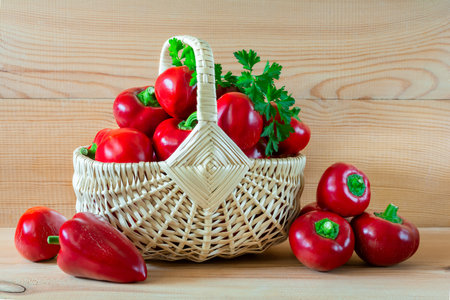 Ripe red peppers in a wicker basket on a wooden tableの写真素材
