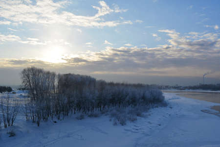 Winter scene with river partially under ice and trees on the bank in the evening