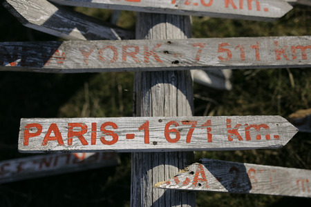 Old wooden signpost on roadmap shows which way and how much left to Paris and New Yourk. It is very old and left on the ground even it has some broken pices but it looks amazing and vintage.の写真素材