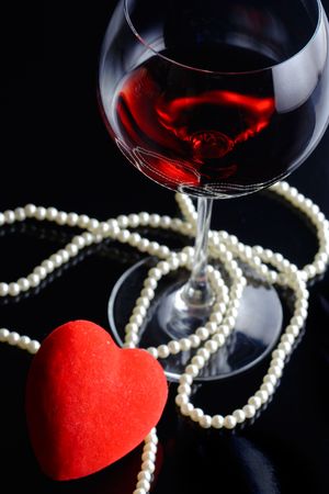 Wine glass and a red heart with pearls against black backgroundの写真素材