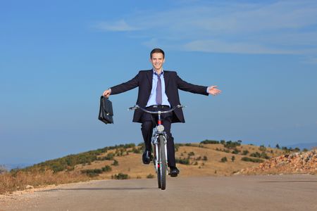 Carefree businessman holding a  briefcase and riding a bicycle outdoorsの写真素材
