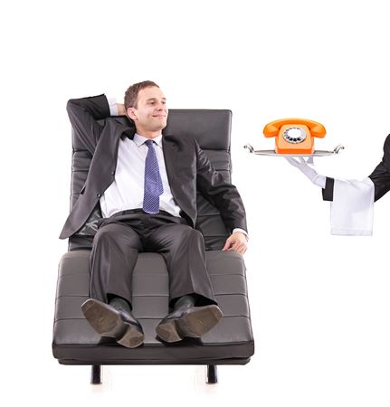 Young businessman relaxing on a sofa while the butler holding a telephone isolated on whiteの写真素材