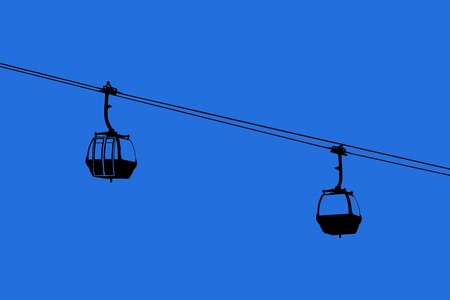 A silhouette of two air-cable cabins against a blue skyの写真素材