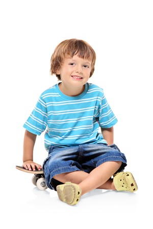 Adorable young boy sitting on a skateboard isolated against white backgroundの写真素材