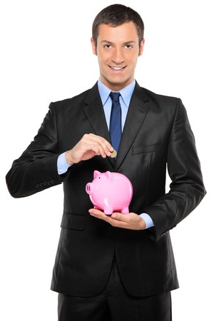 A businessman putting a coin into a pink piggy bank isolated on white backgroundの写真素材