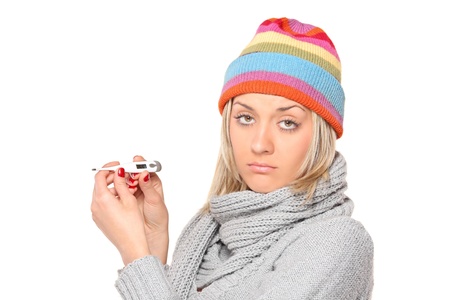 Ill woman wearing a cap and scarf with thermometer in her hands isolated on white backgroundの写真素材