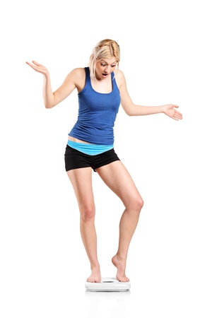 A disapointed young female on a weight scale isolated against white backgroundの写真素材