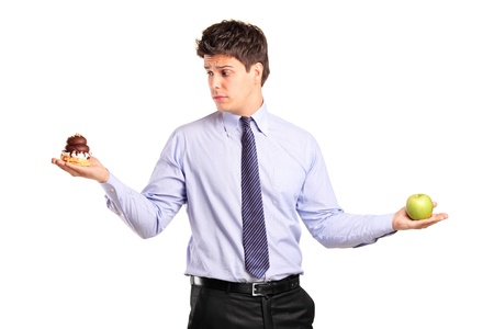 A man holding an apple and slice of cake trying to decide which one to eat isolated on white backgroundの写真素材