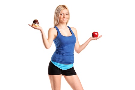 A woman holding an apple and slice of cake trying to decide which one to eat isolated against white backgroundの写真素材