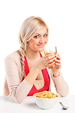 A young female drinking an orange juice and eating cornflakes at breakfast isolated on white backgroundの写真素材