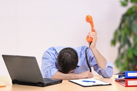 Exhausted businessman with face down holding a telephone in an officeの写真素材