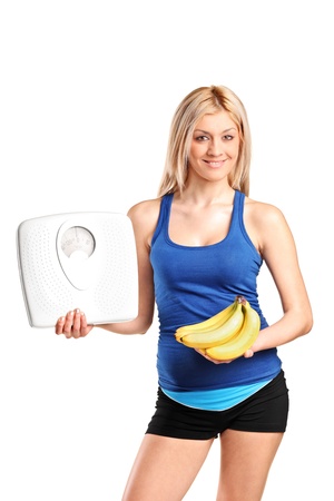 A happy young athlete holding a weight scale and bananas isolated against white backgroundの写真素材