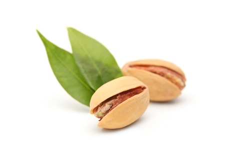 Two salted and roasted pistachio nuts with shell and green leaves isolated on white backgroundの写真素材
