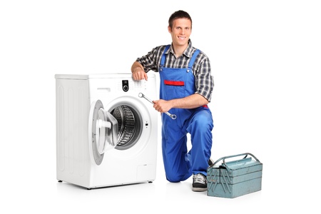 A repairman holding a spanner and posing next to a washing machine isolated on white background の写真素材