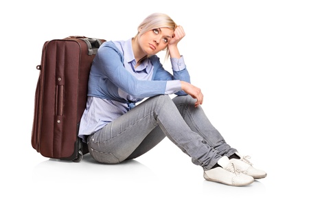 A sad tourist girl seated next to a suitcase isolated on white backgroundの写真素材