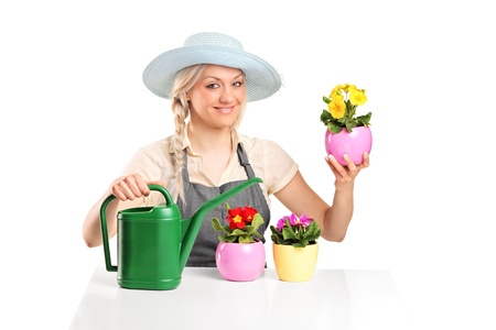 A smiling female gardener posing with flower pots and watering can isolated on white backgroundの写真素材