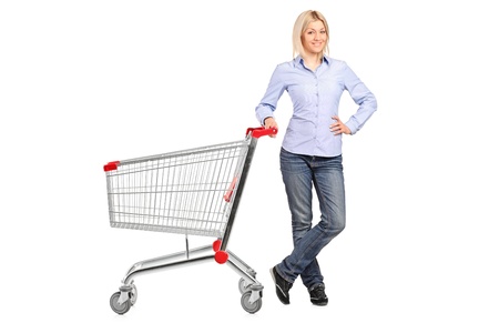 A smiling woman posing next to an empty shopping cart isolated on white backgroundの写真素材