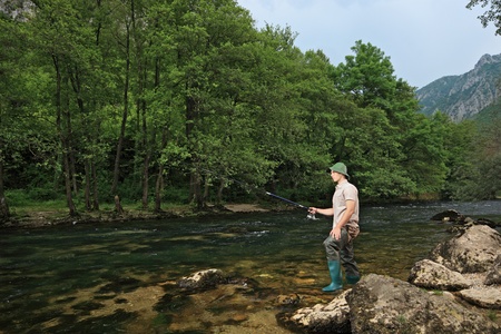 A view of a young fisherman fishing on a river with trees in the backgroundの写真素材