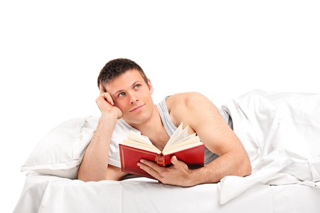 A young thoughtful man with a book lying on his bed isolated on white backgroundの写真素材
