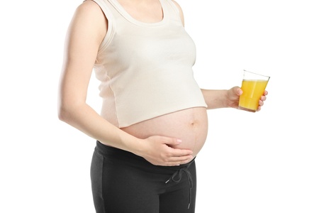 A view of a pregnant woman holding a glass of orange juice isolated on white backgroundの写真素材
