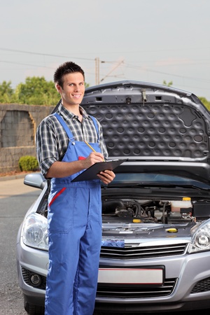 Young mechanic with a clipboard standing next to a car with open hoodの写真素材