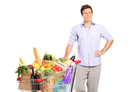 A young male holding a shopping cart full with groceries isolated on white backgroundの写真素材