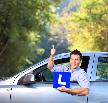 Happy male in his car holding a  L sign and giving thumb up after having his driverの写真素材