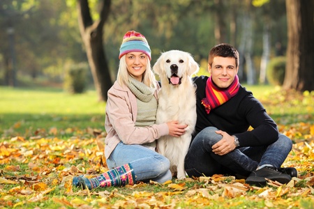 Smiling young man and woman hugging a labrador retreiver dog out in the parkの写真素材