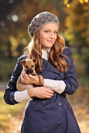 Beautiful young woman smiling and holding a puppy outdoorsの写真素材